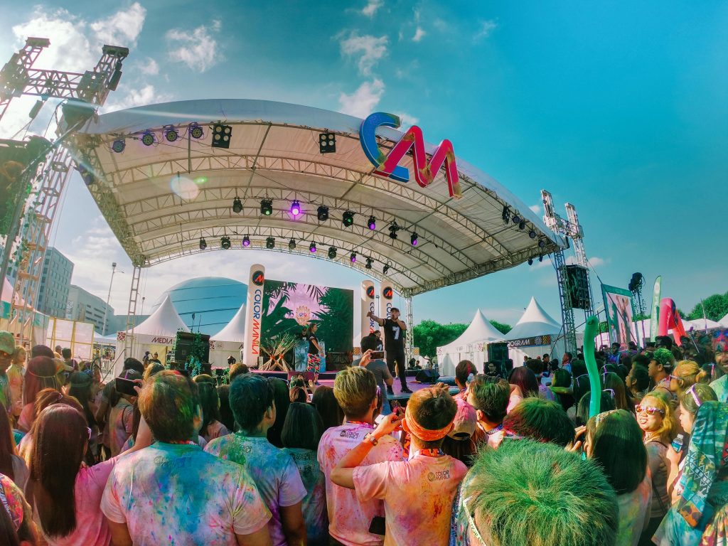 Colorful outdoor music festival with a lively crowd enjoying live performances under a sunny sky.